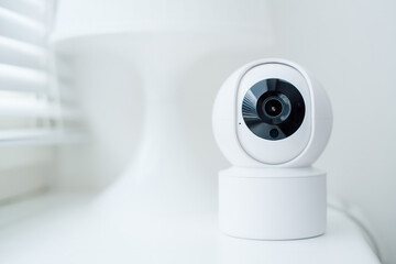 Modern white security camera on a table by a window. Suitable for security system advertisements or residential settings