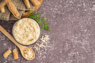 Horseradish sauce in bowl and spoon with ground horseradish on grey background. Top view