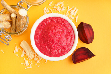 Horseradish sauce with beet in bowl and pieces of beet on yellow background. Top view