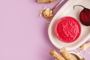 Horseradish sauce with beet in bowl and pieces of beet on lilac background. Top view