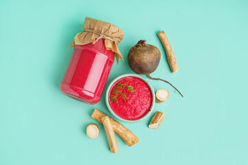 Horseradish sauce with beet in bowl, jar and beetroot on turquoise background. Top view