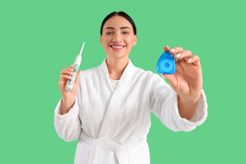Beautiful young happy woman in bathrobe with dental floss and electric toothbrush on green background