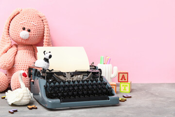 Cute composition with vintage typewriter and knitted toys on table near pink wall