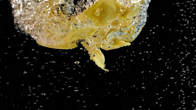 Slow Motion Close-Up Locked Down Shot: Penne Pasta Swirling Underwater with Rising Bubbles on Black Background in 4K Ultra HD Resolution