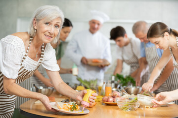 Elderly woman in apron pours sauce into ready dish at cooking master class