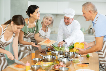 Positive young Asian woman participating group culinary class, engrossed in cooking process talking...