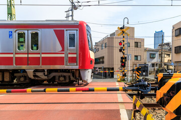 遮断機のある踏切を通過する赤い通勤電車