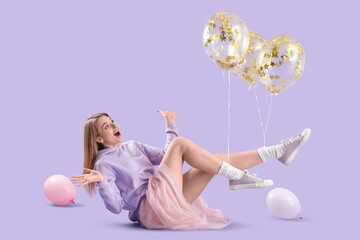 Young woman with balloons lying on lilac background