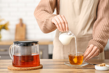 Young woman pouring milk in cup of tea in kitchen