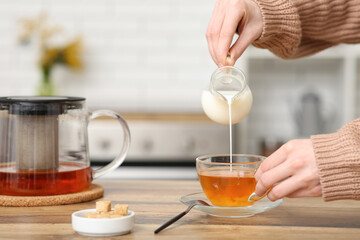 Young woman pouring milk in cup of tea in kitchen