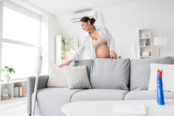 Young pregnant woman fluffing cushion at home