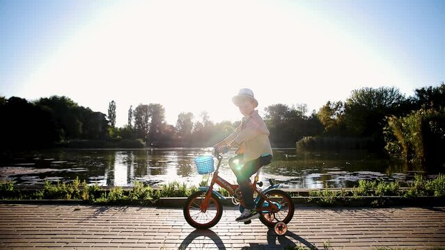 Kid is learning to ride bike. Child rides bicycle on rural road. Cheerful boy ridding on bike in summer park
