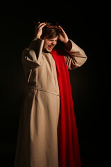 Man in Jesus robe and crown of thorns screaming with light on black background