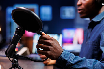 Black man uses professional mic to record a podcast in home studio. Close up shows african american...
