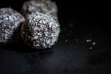 Chocolate truffles with coconut sprinkles on a black background, macro photography, details
