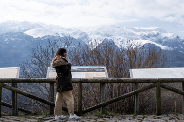 Fototapeta na wymiar Young lady with brown hair, green coat, admires stunning snowy mountain vista.