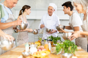 Smiling elderly man, seasoned professional chef conducting culinary courses, imparting cooking...