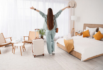 Happy female tourist with suitcase in hotel room