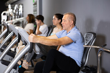 Fototapeta na wymiar Portrait of active elderly man doing cardio training, cycling on stationary bike in gym ..