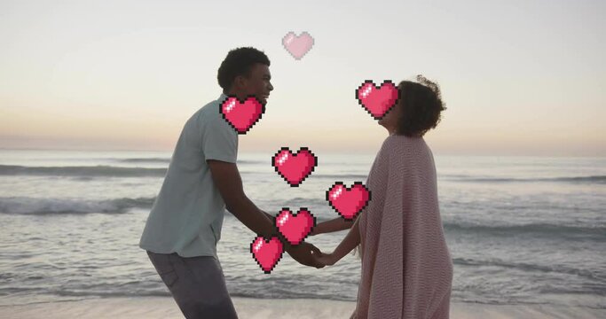 Animation of hearts moving over diverse couple in love holding hands on beach in summer