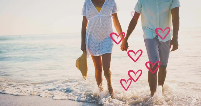 Animation of hearts moving over diverse couple in love holding hands on beach in summer