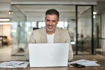 Fototapeta na wymiar Busy smiling middle aged professional business man executive investor ceo leader using computer working with online finances sitting at desk. Happy mature bank manager looking at laptop in office.