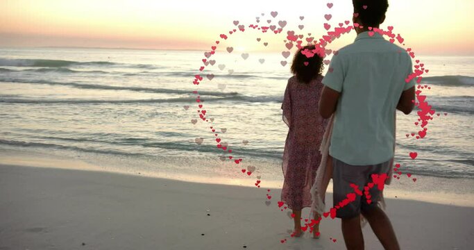 Animation of hearts moving over diverse couple in love dancing on beach in summer