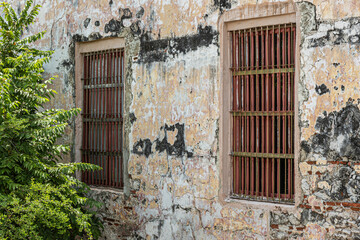 Cartagena, Colombia - July 25, 2023:Couple of grilled windows in ancient wall on Baluarte de San Ignacio rampart and bastion. Some green foliage