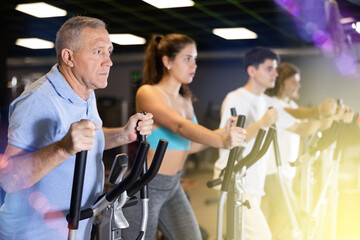 Group of athletic people of different ages train on elliptical trainers steppers