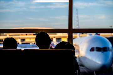 Silhouette of two young adults slouched in an airport terminal with a defocused airplane out the window 
