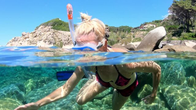 Split-view of a female snorkeler exploring the clear waters of Saint Andrew beach of Elba island, capturing both above and underwater scenes. Tuscan archipelago of mediterranean sea in Italy.