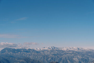 Snow-covered mountain range above the Bay of Kotor against the blue sky in winter. Montenegro