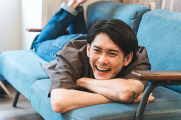 家のリビングでくつろぐ笑顔の若いアジア人・日本人男性（リラックス）
