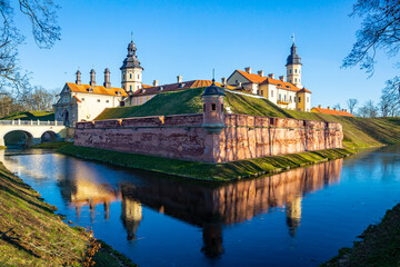 Winter view of belarusian medieval Nesvizh Castle with park and ponds on sunny day - obrazy, fototapety, plakaty