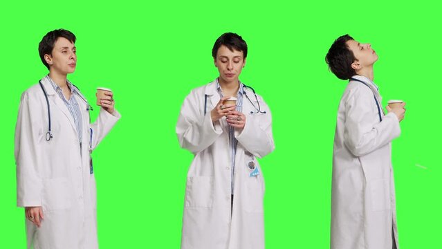 Happy medic serving hot coffee cup as refreshment against greenscreen backdrop, wearing white coat and drinking caffeine beverage. General practitioner enjoying drink, medical expertise. Camera B.