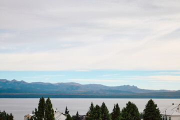 buildings on the shore in a thicket of trees, against the backdrop of a lake and mountains