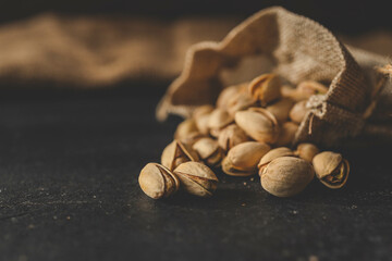 Pistachios spill out of burlap on a black background