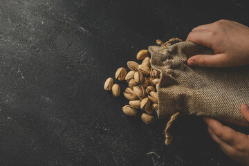 Pistachios spill out of burlap on a black background