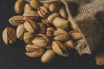 Pistachios spill out of burlap on a black background