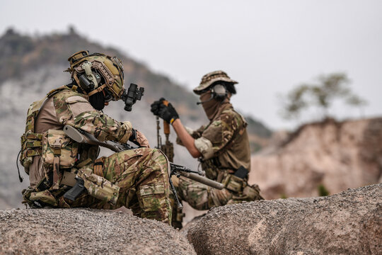 Soldiers in camo gear during a tactical operation with binoculars and rifles on a rocky terrain, showcasing military precision and readiness. - Powered by Adobe