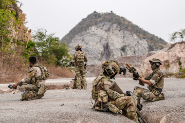 Soldiers in camo gear during a tactical operation with binoculars and rifles on a rocky terrain, showcasing military precision and readiness.