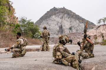 Soldiers in camo gear during a tactical operation with binoculars and rifles on a rocky terrain, showcasing military precision and readiness.