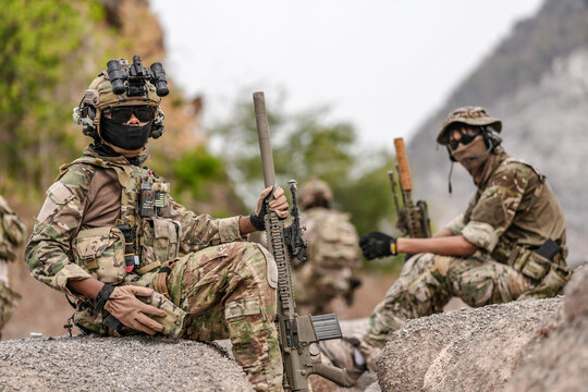 Soldiers in camo gear during a tactical operation with binoculars and rifles on a rocky terrain, showcasing military precision and readiness.