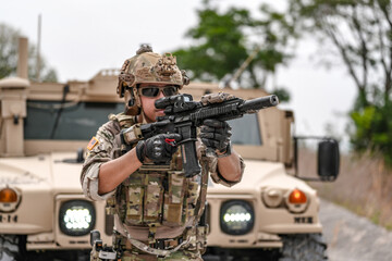 Confident soldier in full gear stands before a military vehicle, rifle in hand, showcasing...