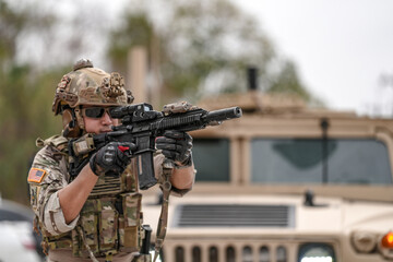Confident soldier in full gear stands before a military vehicle, rifle in hand, showcasing readiness and strength.