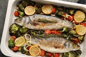 Delicious fish with vegetables and lemon in baking dish on grey table, top view