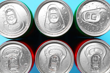 Energy drinks in wet cans on light blue background, top view