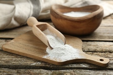 Baking powder in scoop and bowl on wooden table, closeup