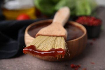 Marinade in bowl and basting brush on brown table, selective focus