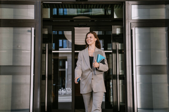 Businesswoman exiting building with notebooks and smartphone.